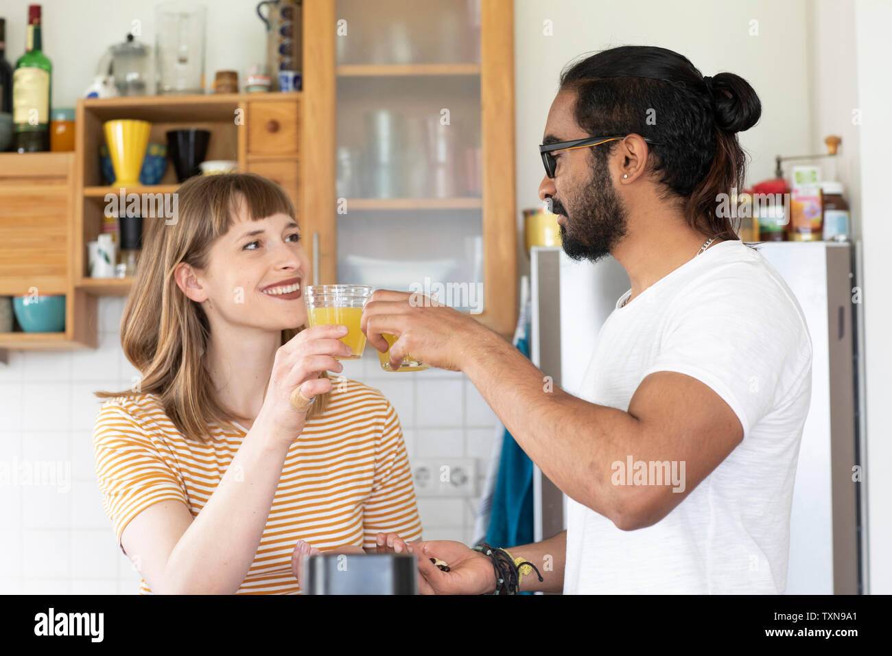 Multi-ethnic couple toasting with juice in kitchen Stock Photo