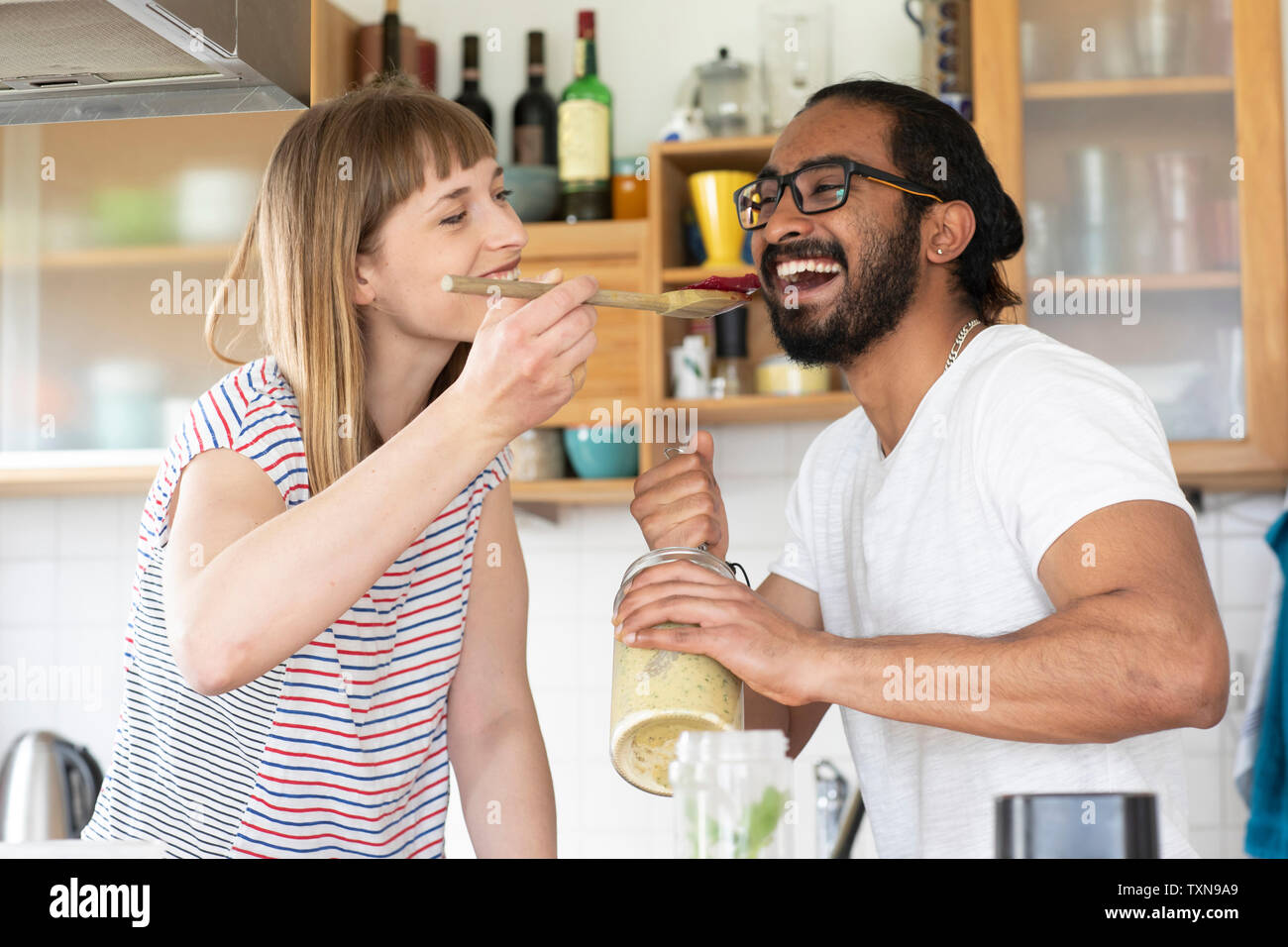 Woman feeding man with wooden spoon in kitchen Stock Photo