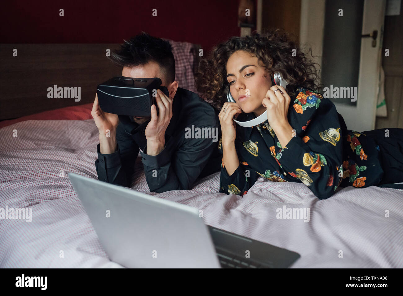 Couple using VR headset and laptop on bed Stock Photo