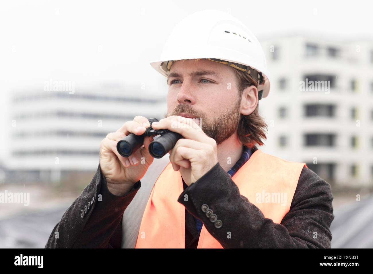 Mid adult male civil engineer holding binoculars on construction site Stock Photo