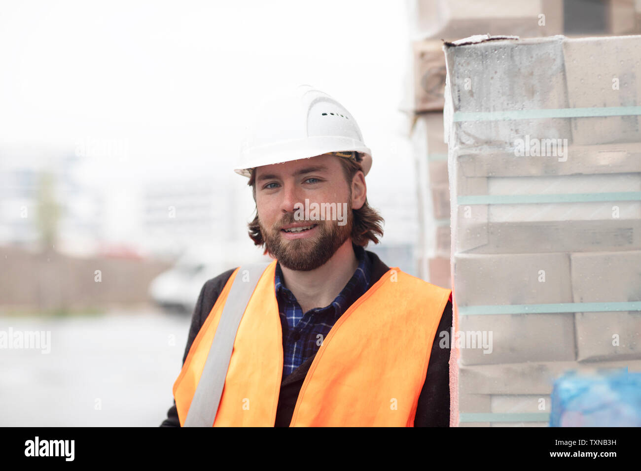 Mid adult male civil engineer leaning against stacked building material on construction site, portrait Stock Photo