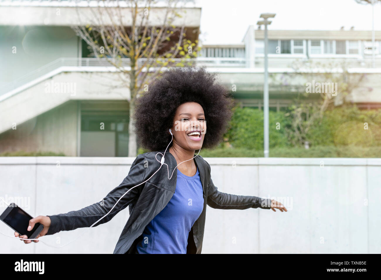 Happy young woman with afro hair in city, laughing and dancing to ...