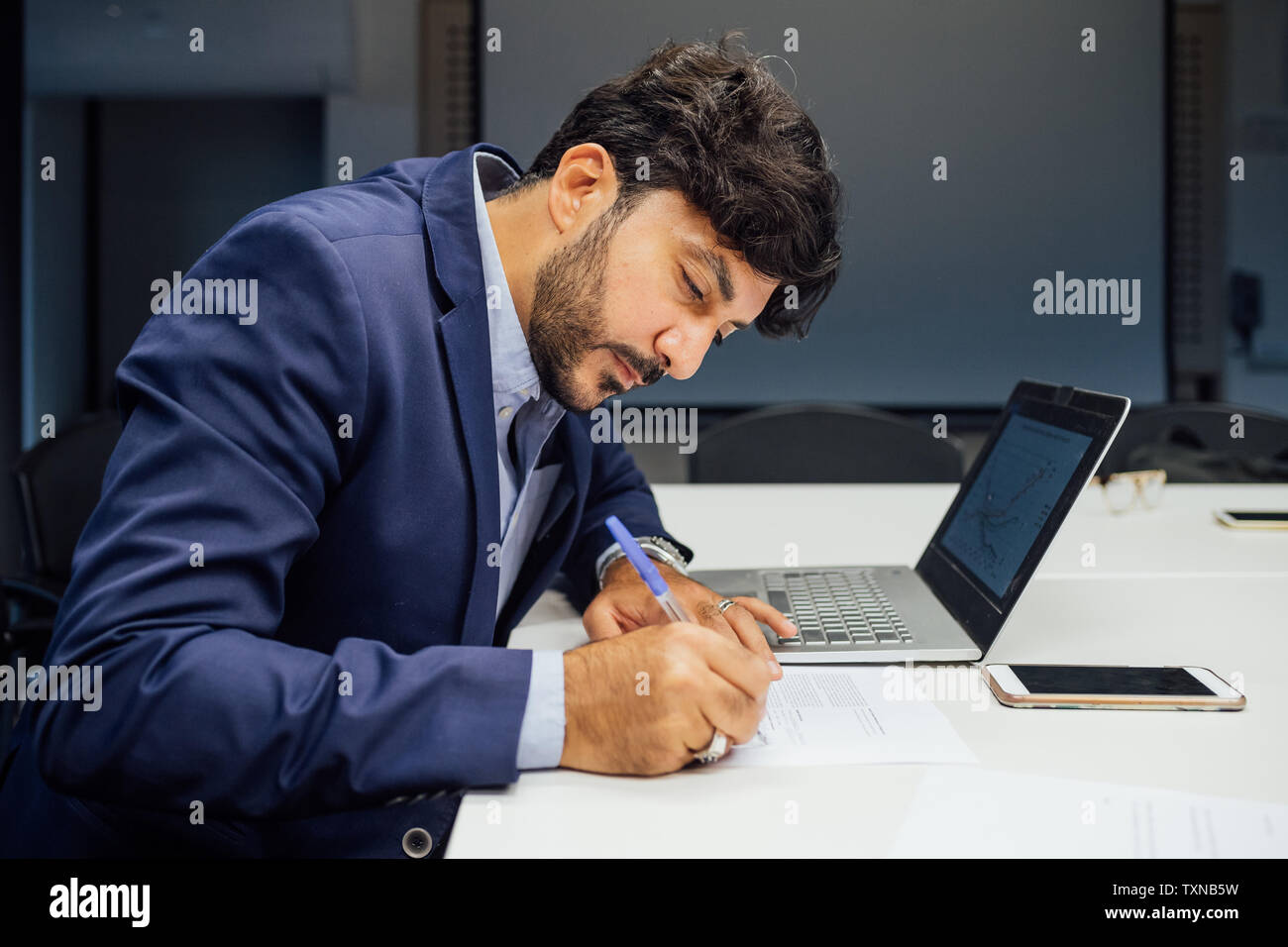 Businessman writing notes and using laptop in office Stock Photo