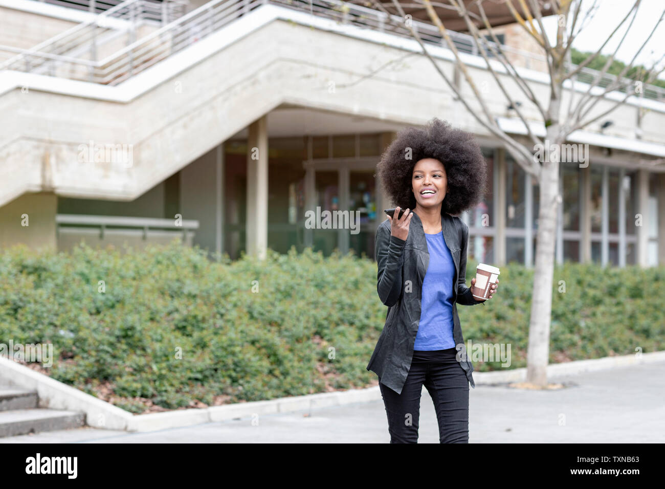 Young woman with afro hair in city, walking and talking to smartphone Stock Photo