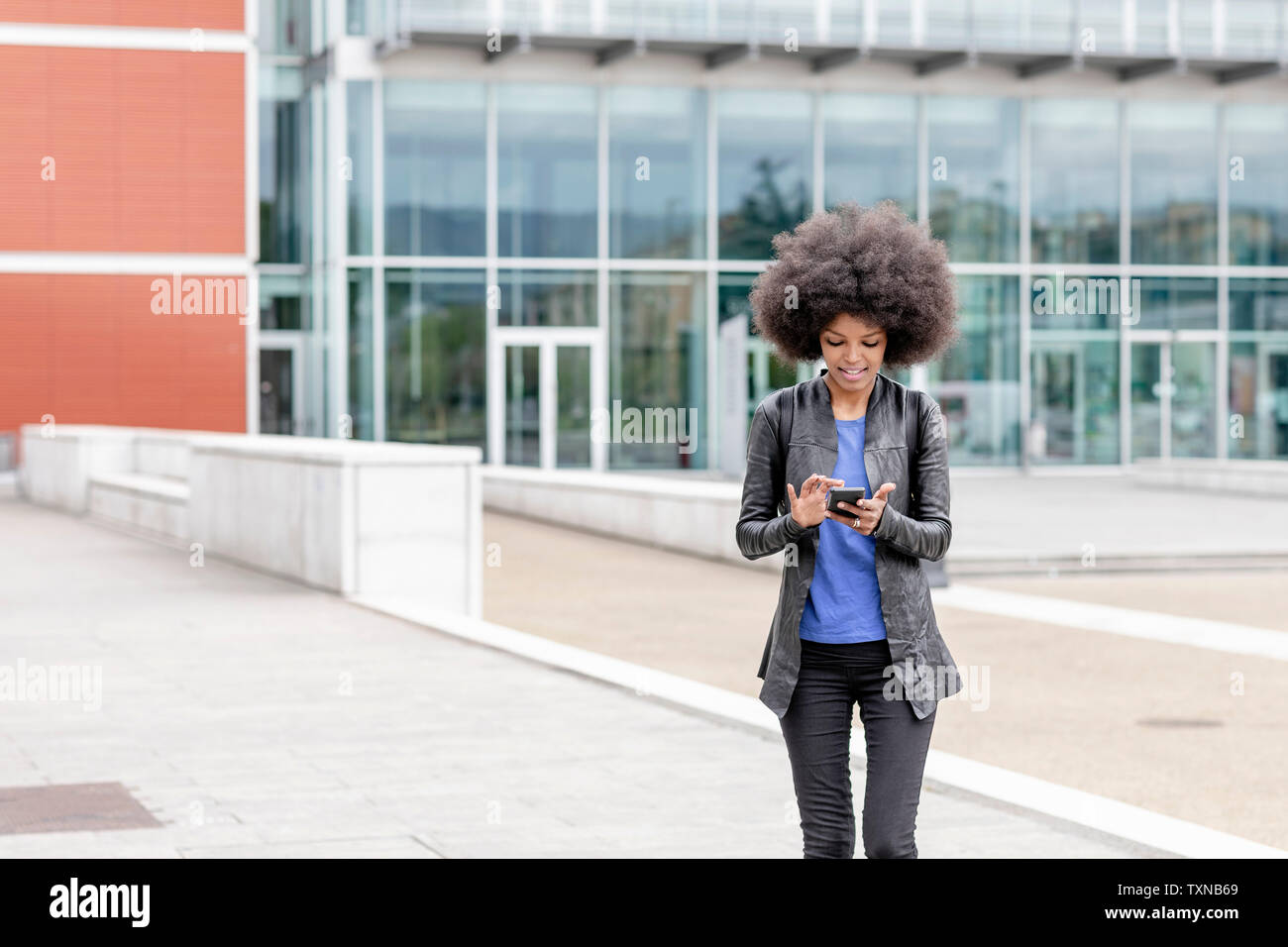 Young woman with afro hair in city, using smartphone touchscreen Stock Photo