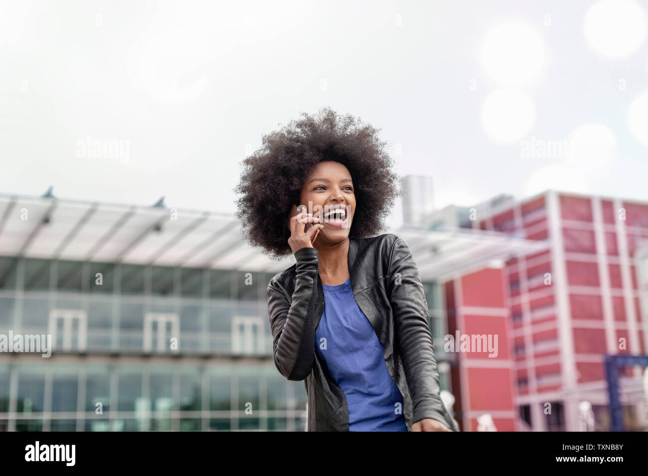 Happy young woman with afro hair in city, laughing and making smartphone call Stock Photo