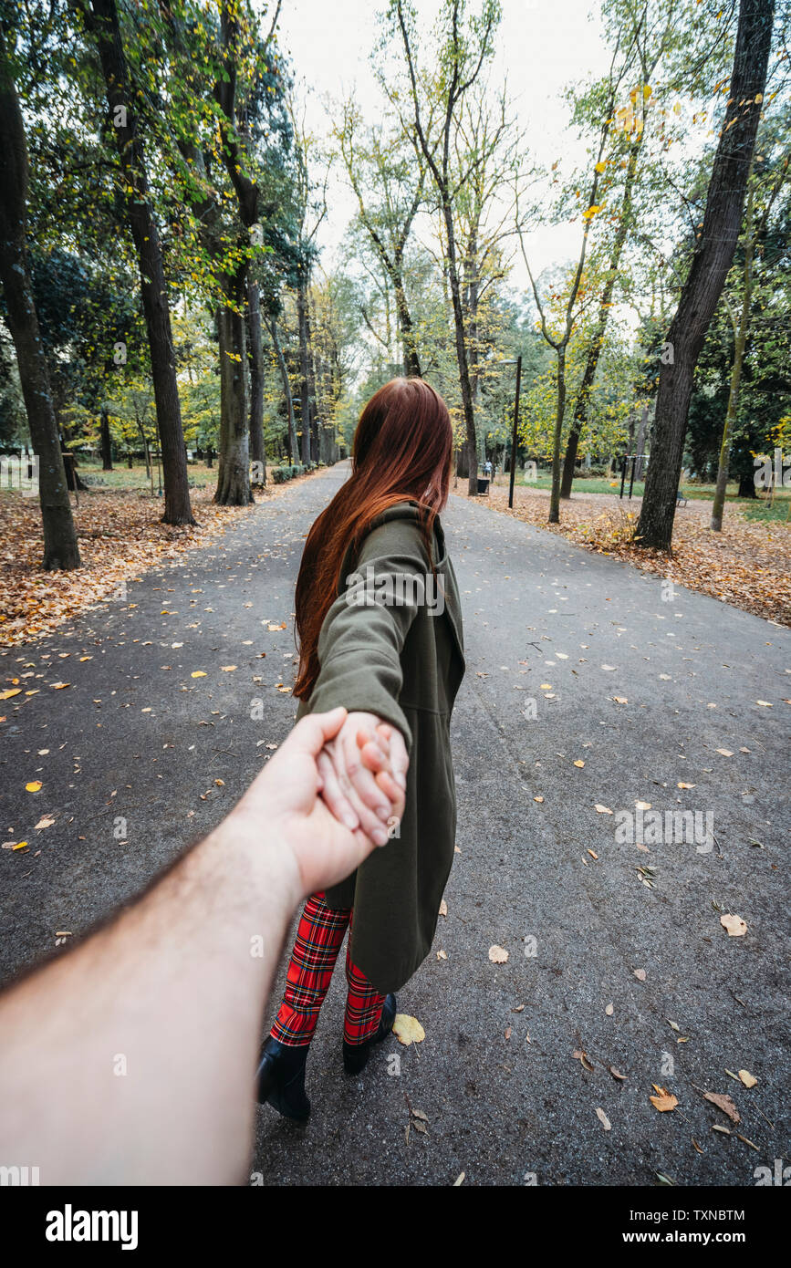 Young woman with long red hair holding boyfriend's hand in autumn park, personal perspective Stock Photo