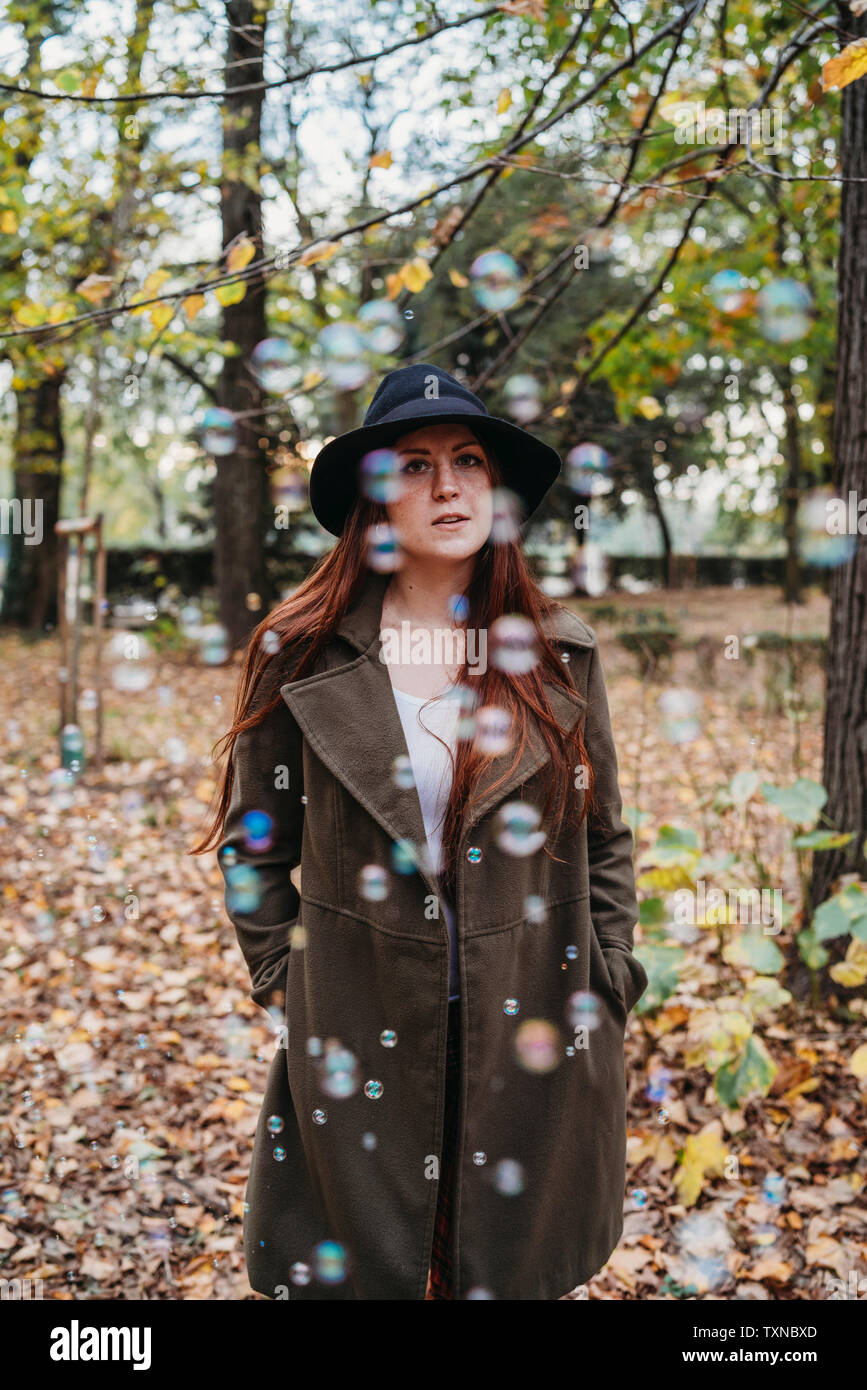 Young woman with long red hair amongst floating bubbles in autumn park, portrait Stock Photo