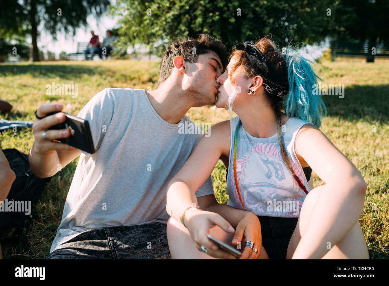 Couple kissing, using smartphone in park Stock Photo