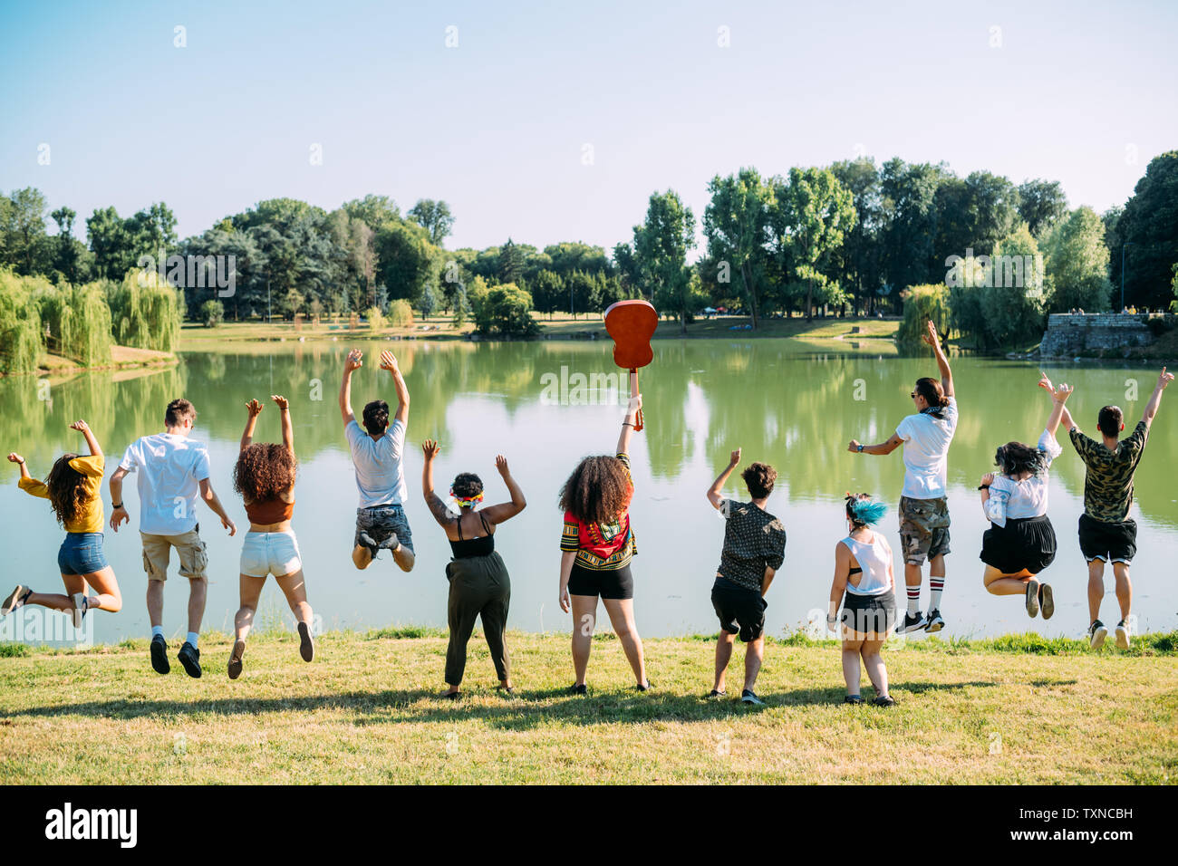 Group of friends jumping in front of lake in park Stock Photo - Alamy