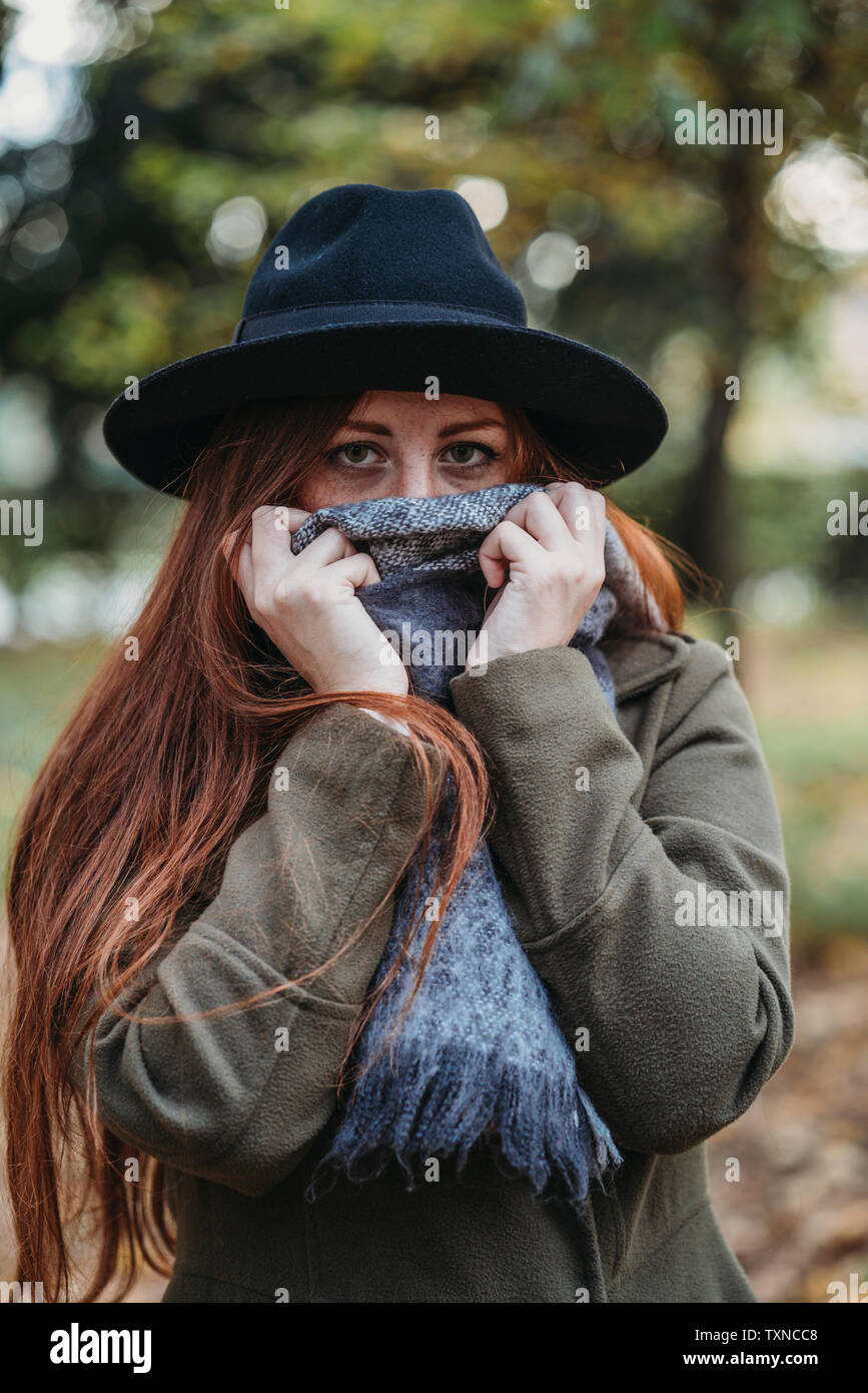 Young woman with long red hair in autumn park covering mouth with scarf, portrait Stock Photo