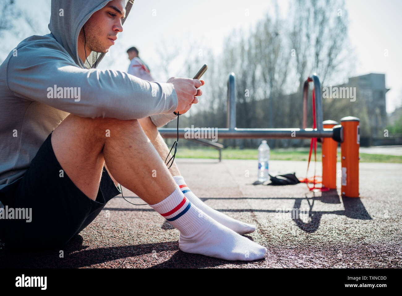 Calisthenics class at outdoor gym, young man sitting down and looking at smartphone Stock Photo