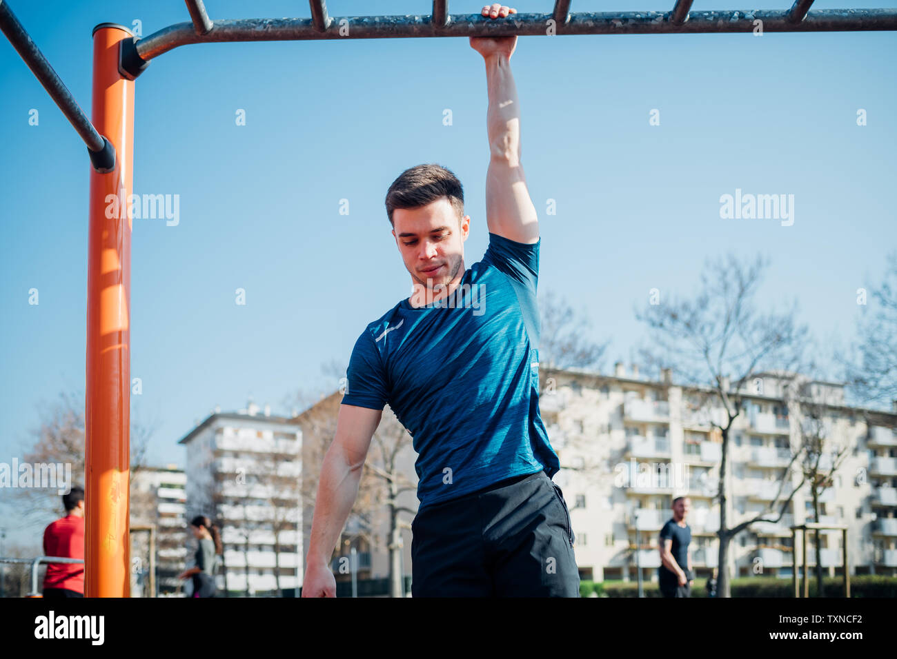 Calisthenics at outdoor gym, young man hanging by one arm from exercise equipment Stock Photo