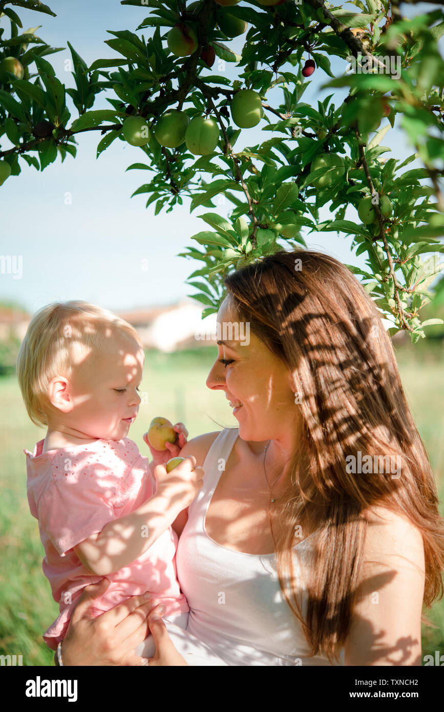 Mother gazing at toddler daughter under fruit tree, Arezzo, Tuscany, Italy Stock Photo