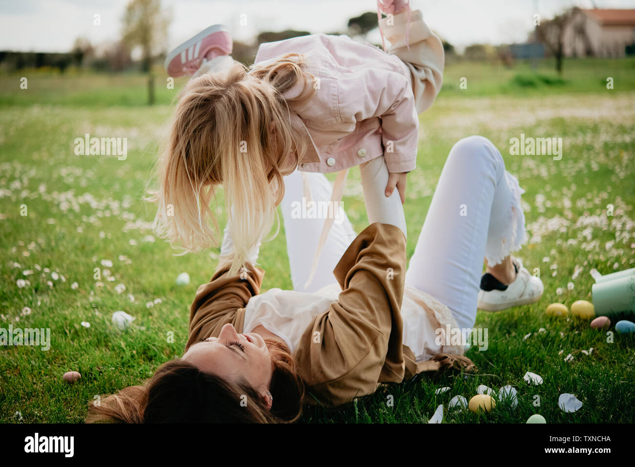 Mother lying on back holding up daughter in wildflower field after easter egg hunt, Arezzo, Tuscany, Italy Stock Photo