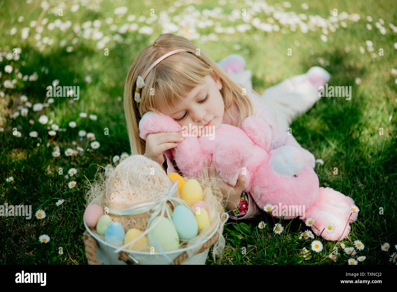 Cute girl lying on grass with toy rabbit and easter egg basket Stock Photo