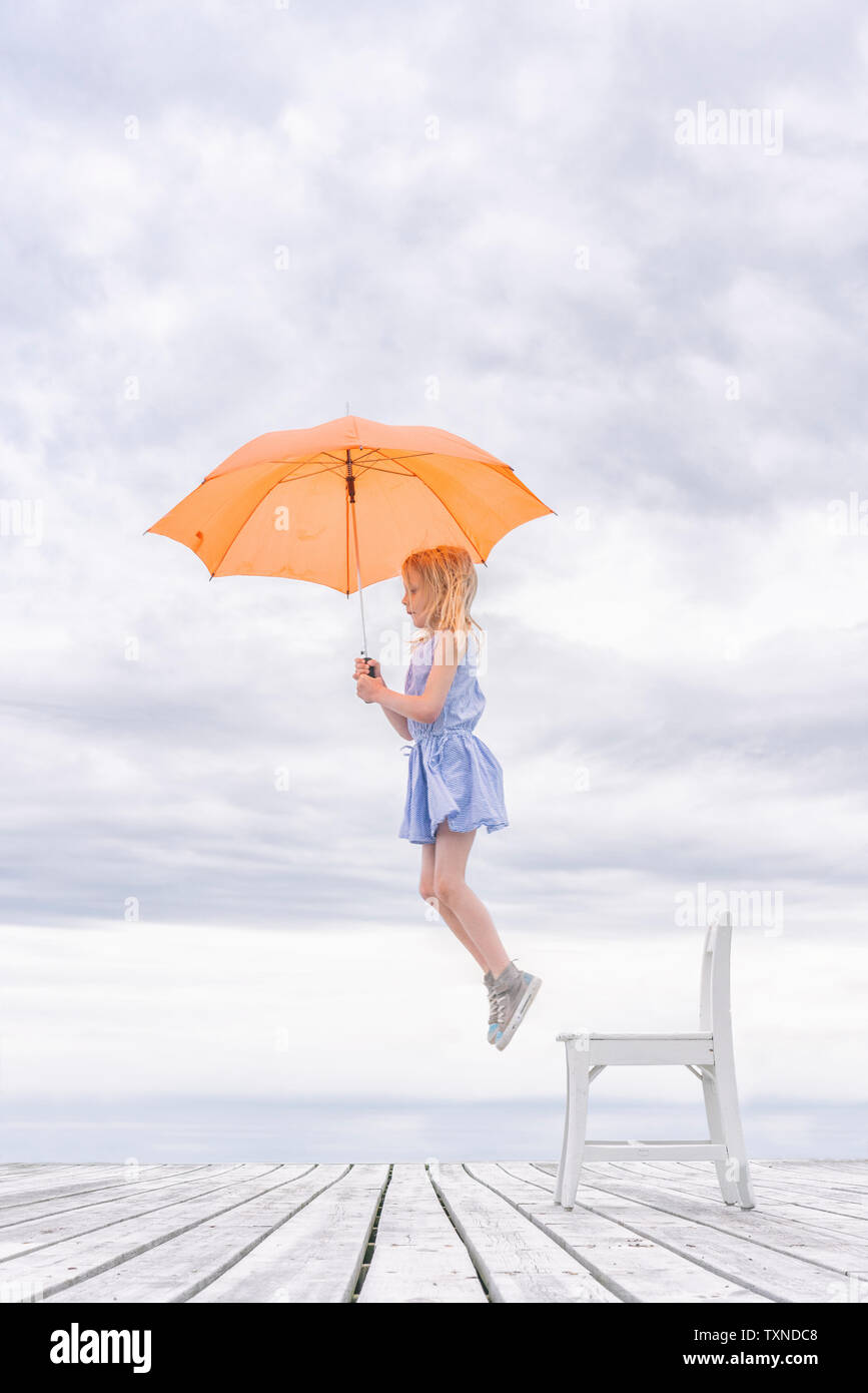 Girl being lifted off her chair by umbrella Stock Photo