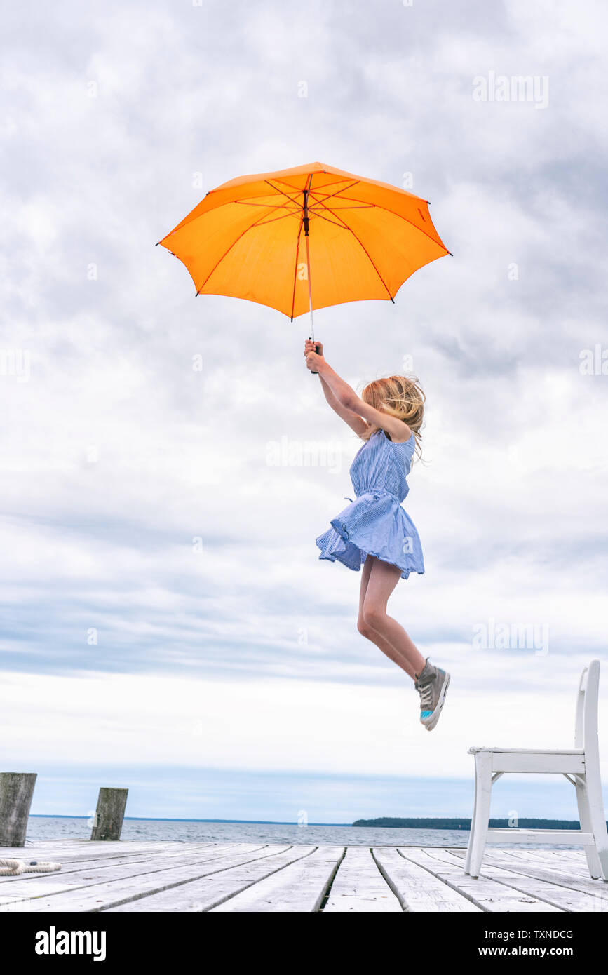 Girl being lifted off her chair by umbrella Stock Photo