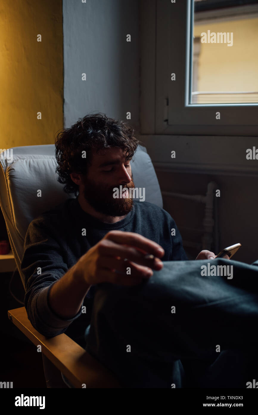 Bearded young man using smartphone at home Stock Photo