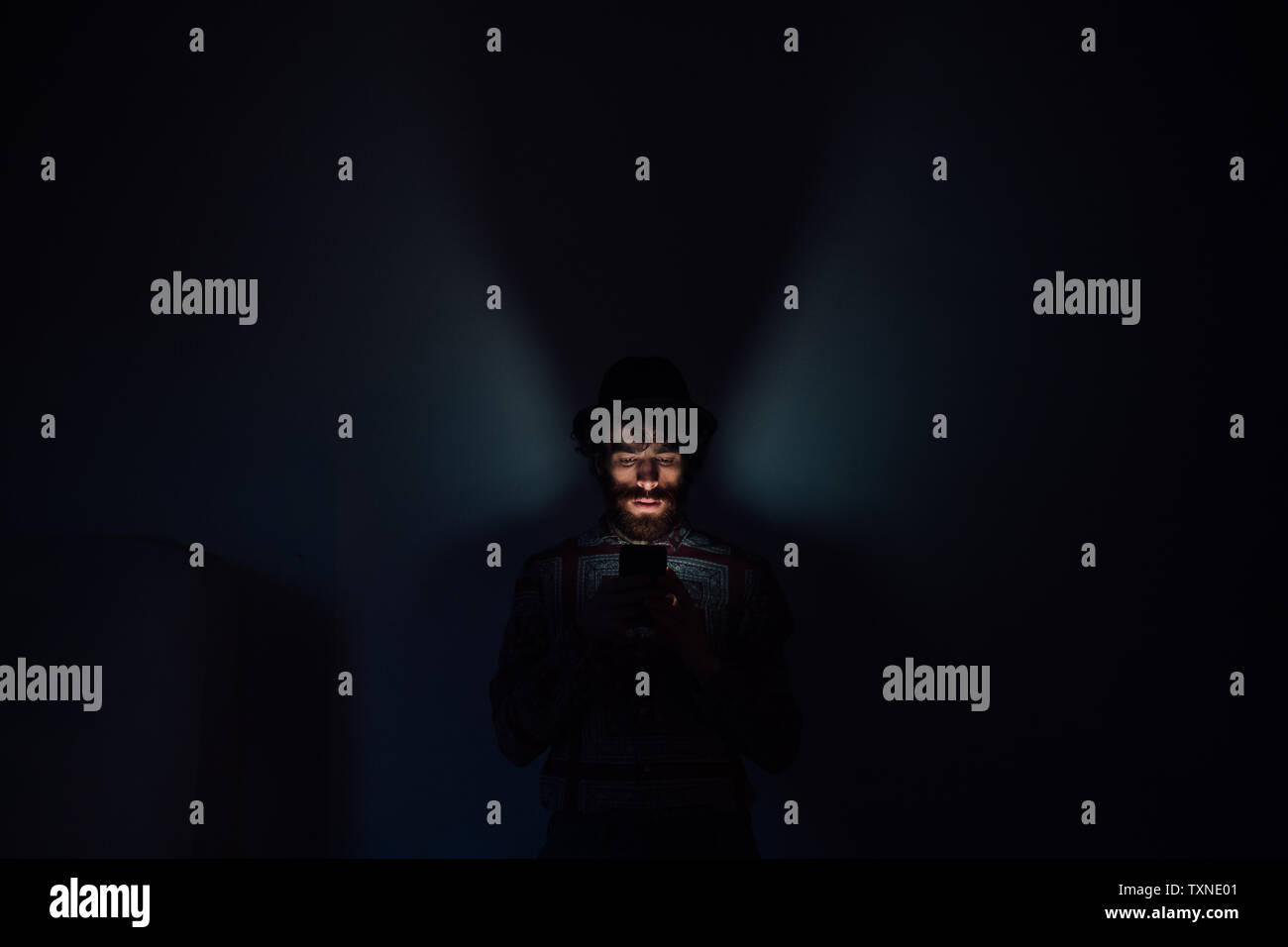 Bearded young man using smartphone in dark room Stock Photo