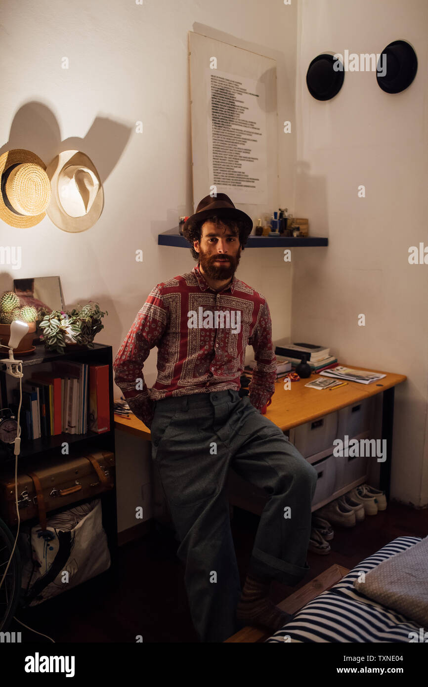 Bearded young man sitting on bedroom table Stock Photo