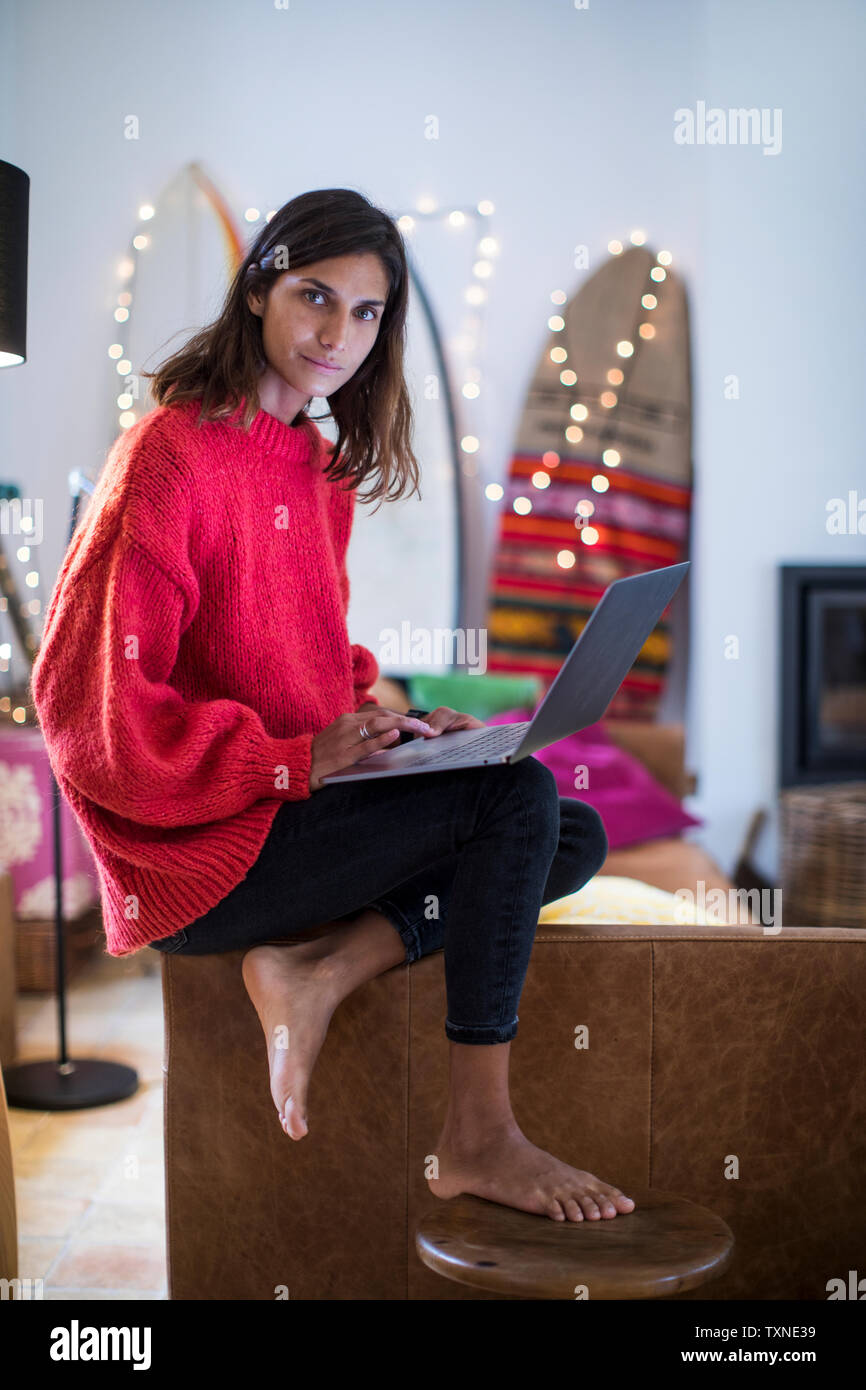 Young woman in red sweater on living room sofa using laptop, portrait