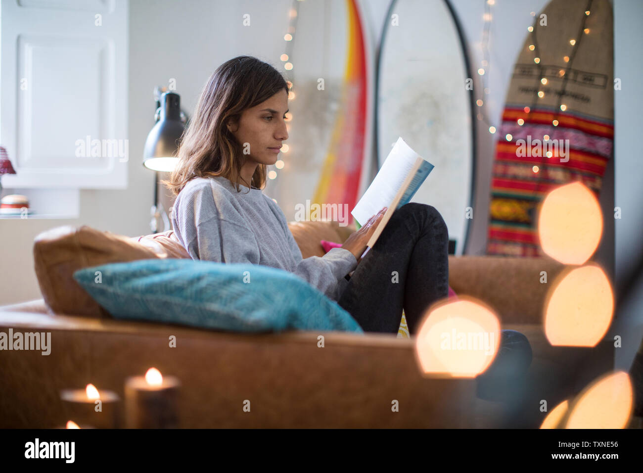 Young woman sitting on living room sofa reading a book Stock Photo - Alamy