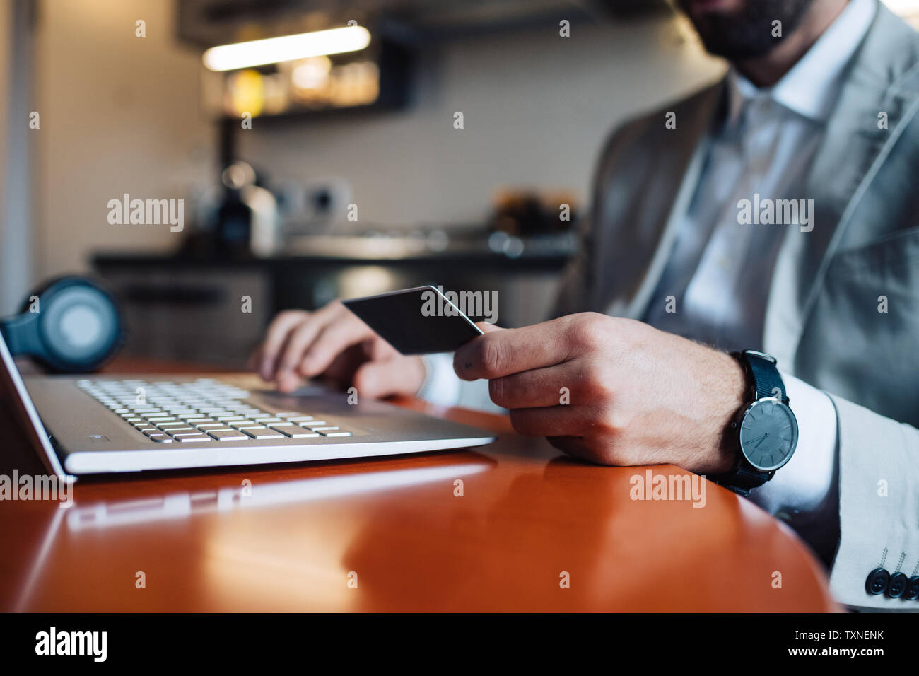 Mid adult man sitting at kitchen table with laptop and credit card, cropped Stock Photo