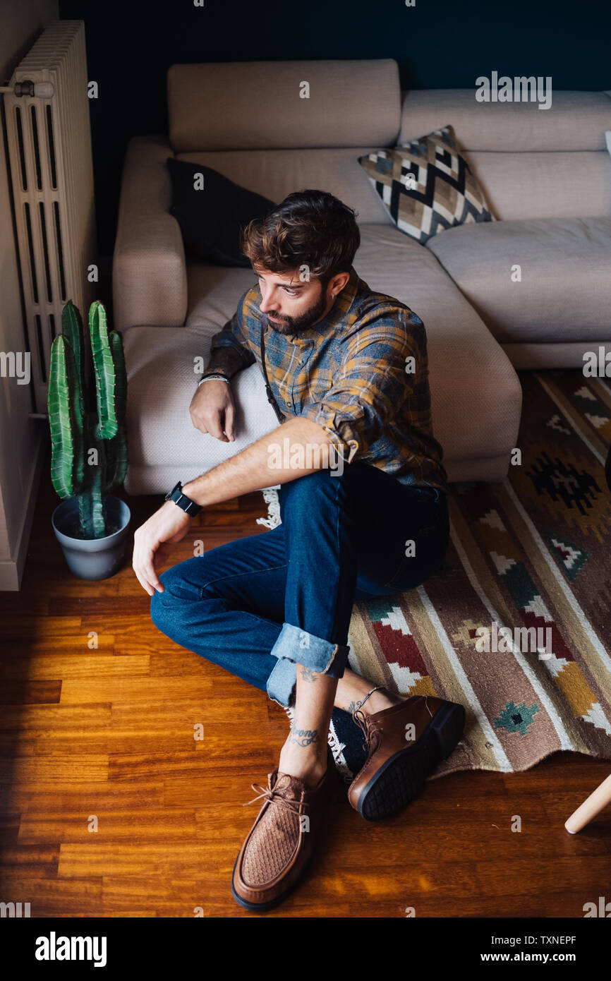 Mid adult man sitting on living room floor looking out through window Stock Photo