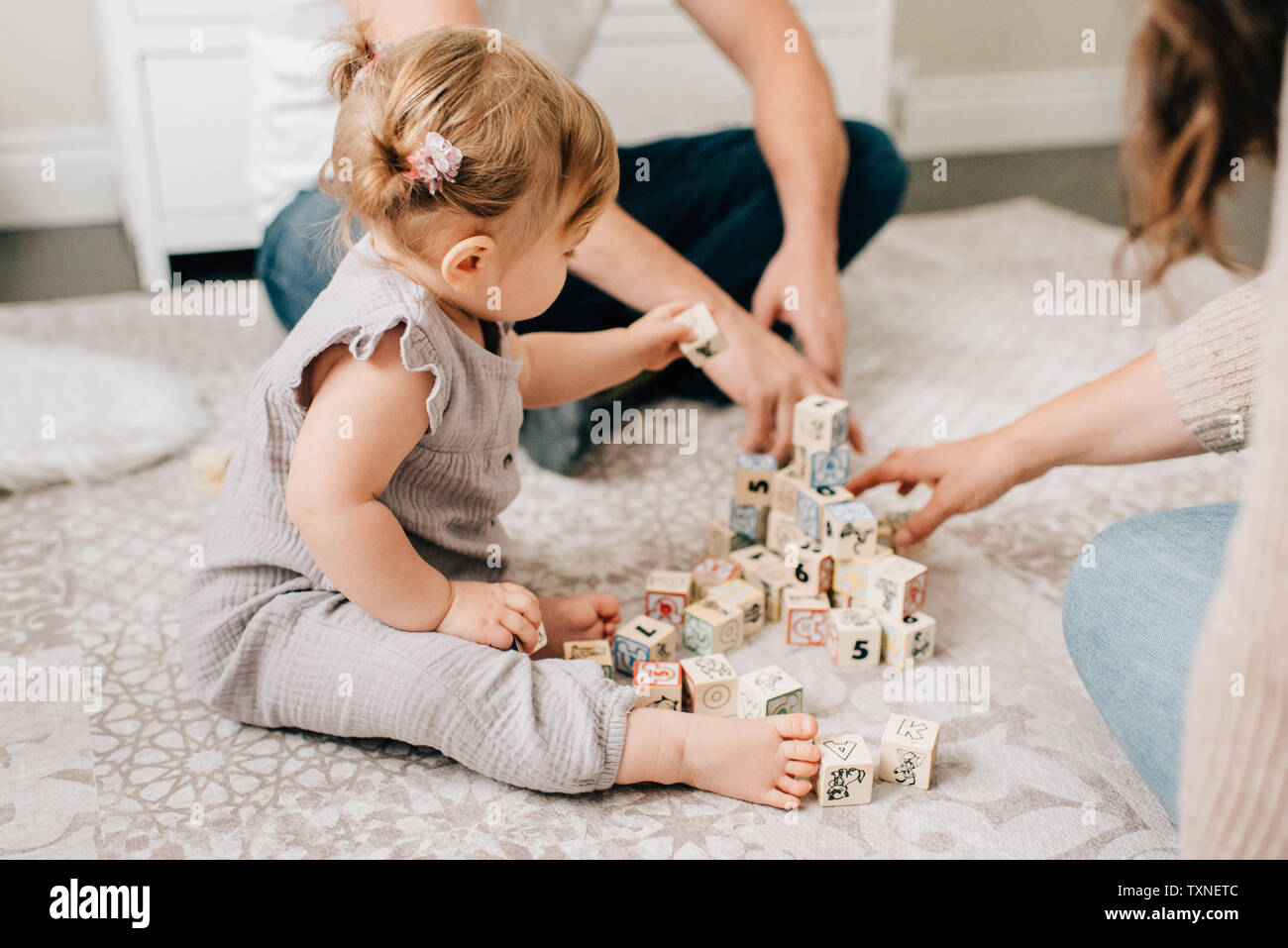 Mother and father on nursery floor with baby daughter playing with ...