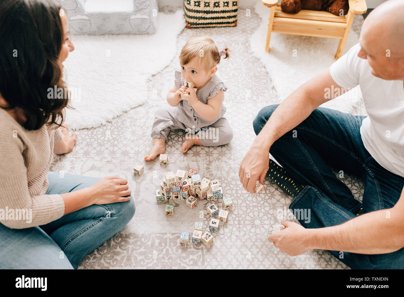 Mother and father sitting on nursery floor with baby daughter playing ...