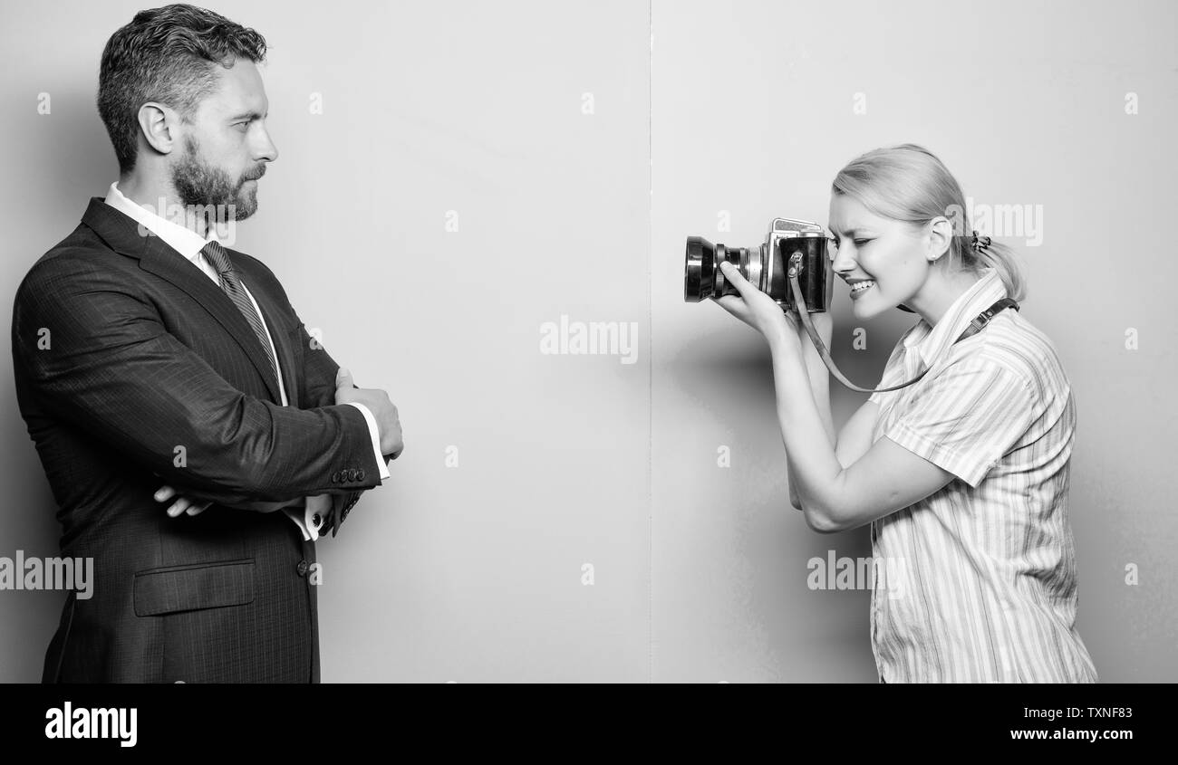 His confidence is her focus. Photographer shooting male model in studio. Businessman posing in front of female photographer. Fashion shooting in photo studio. Pretty woman using professional camera. Stock Photo