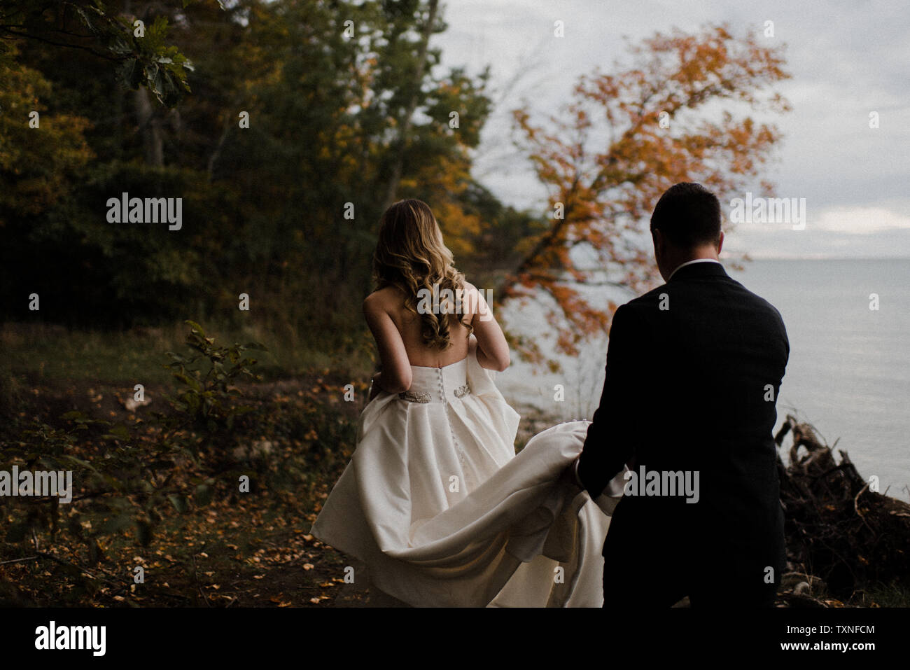Romantic young groom carrying bride's wedding dress train on lakeside