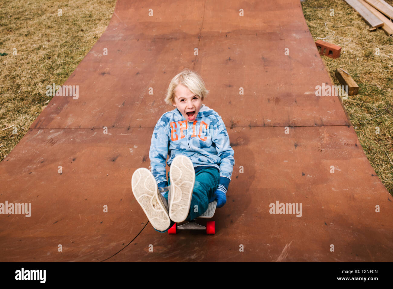 Boy sitting and skateboarding backwards down wooden skateboard ramp