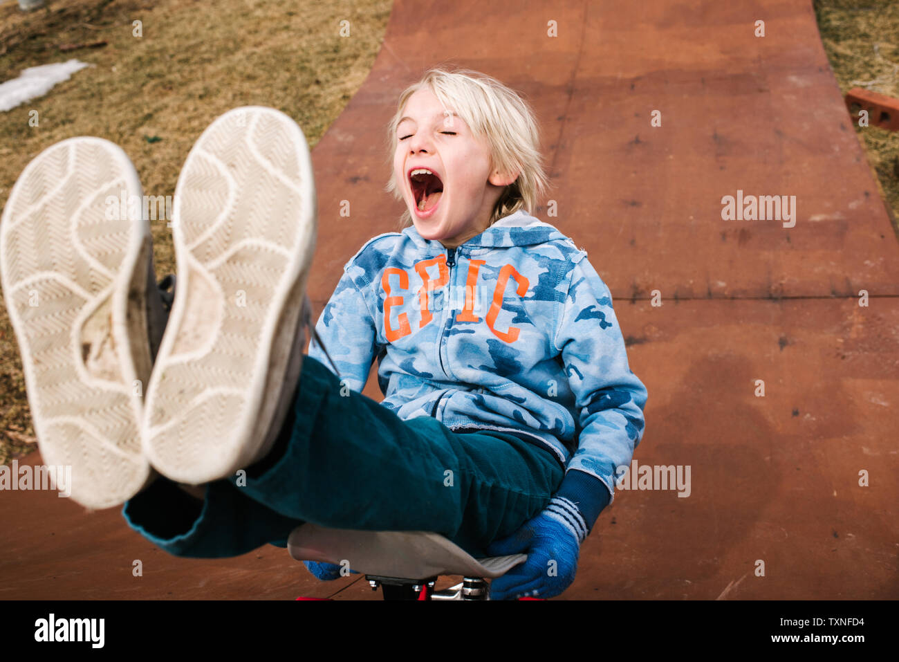 Boy sitting and skateboarding backwards down wooden skateboard ramp Stock Photo Alamy