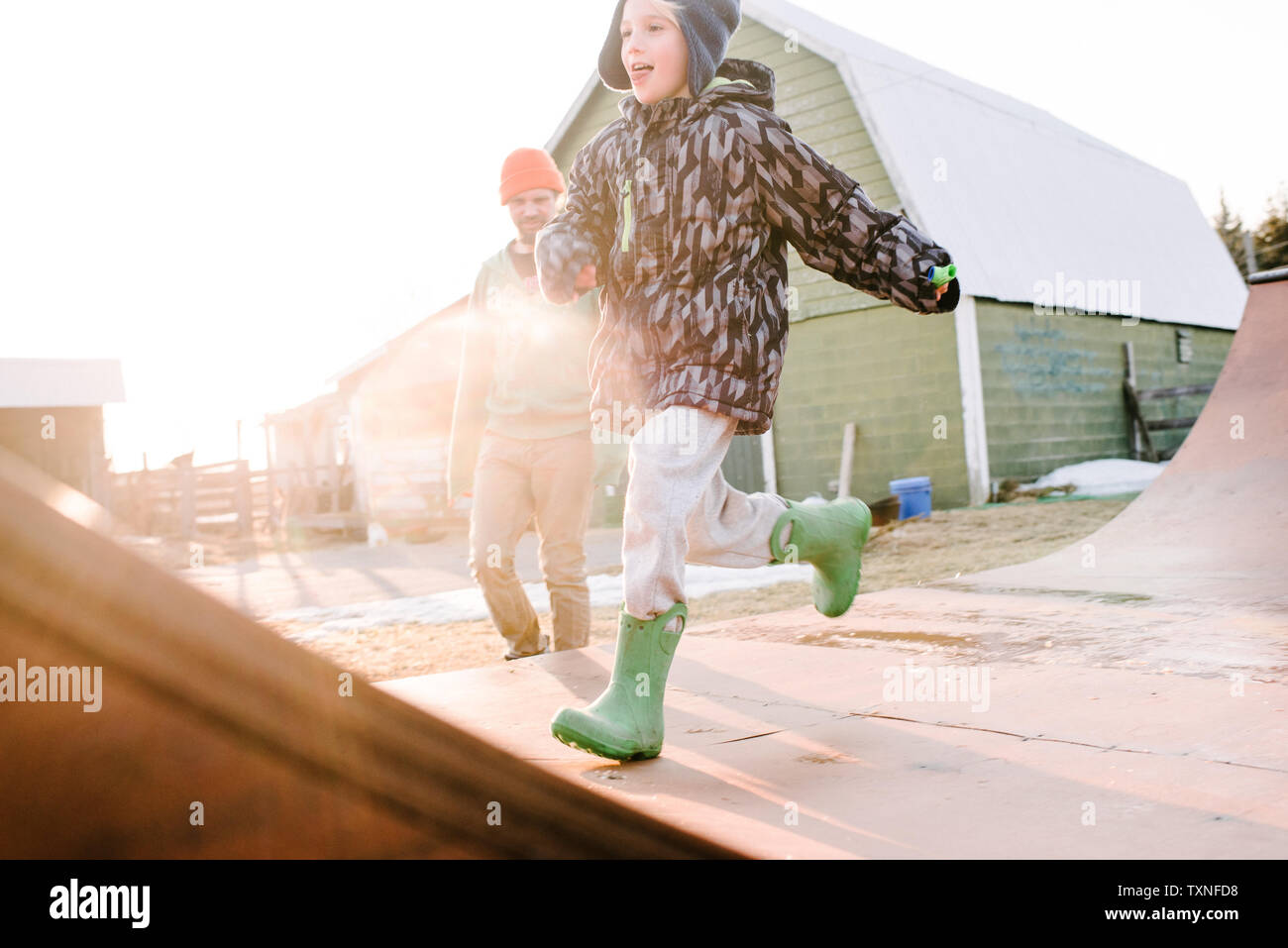 Boy with father running on sunlit farmyard skateboard ramp Stock Photo
