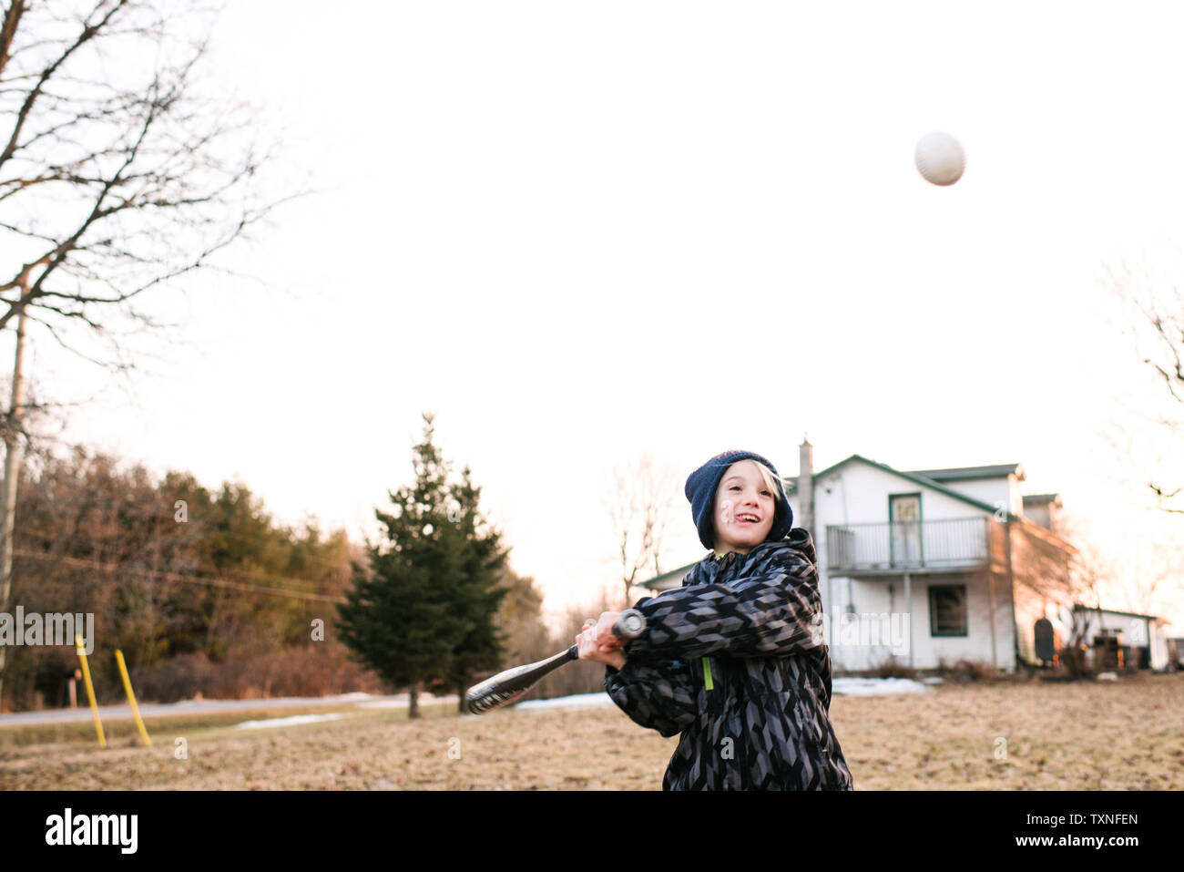 Boy hitting baseball ball in rural field, action Stock Photo