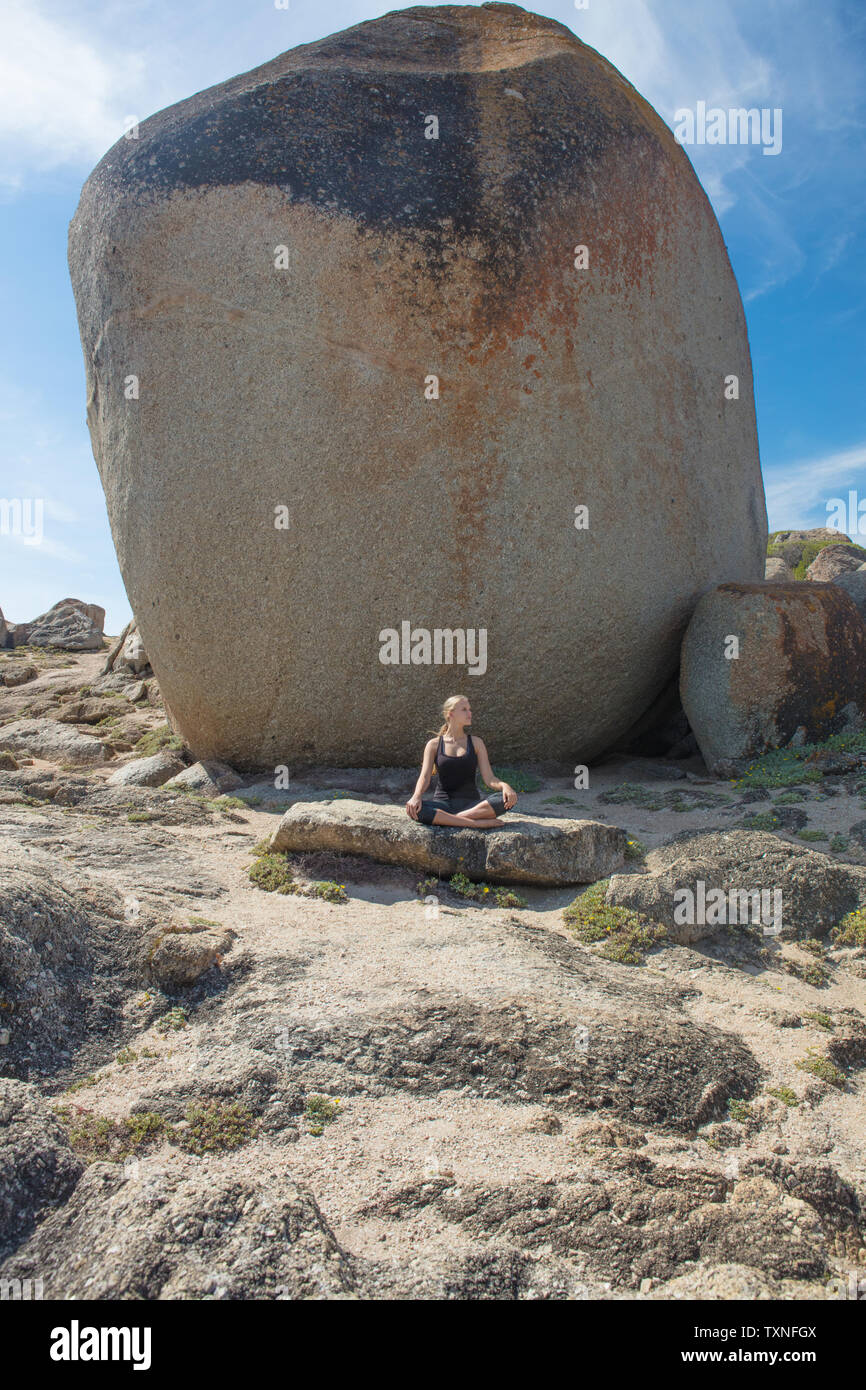 Young woman practicing lotus yoga pose on beach rock, Cape Town