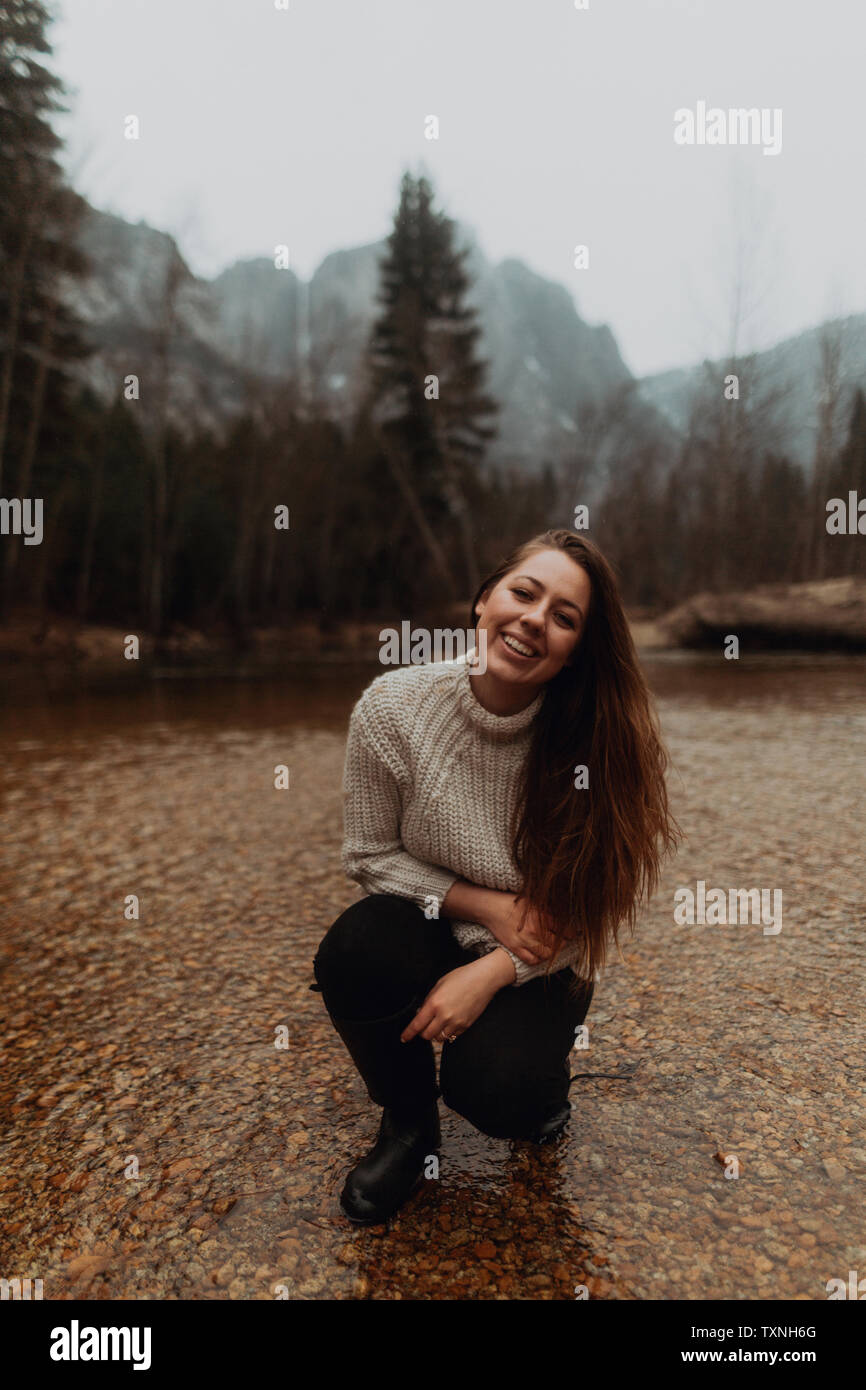 Young woman crouching in river, portrait, Yosemite Village, California, USA Stock Photo