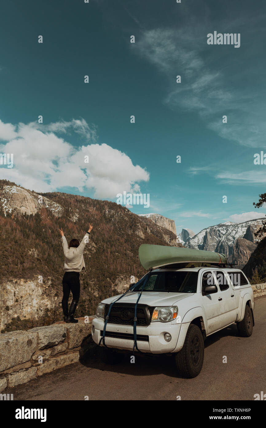 Young woman on top of roadside wall with hands raised, rear view, Yosemite Village, California, USA Stock Photo