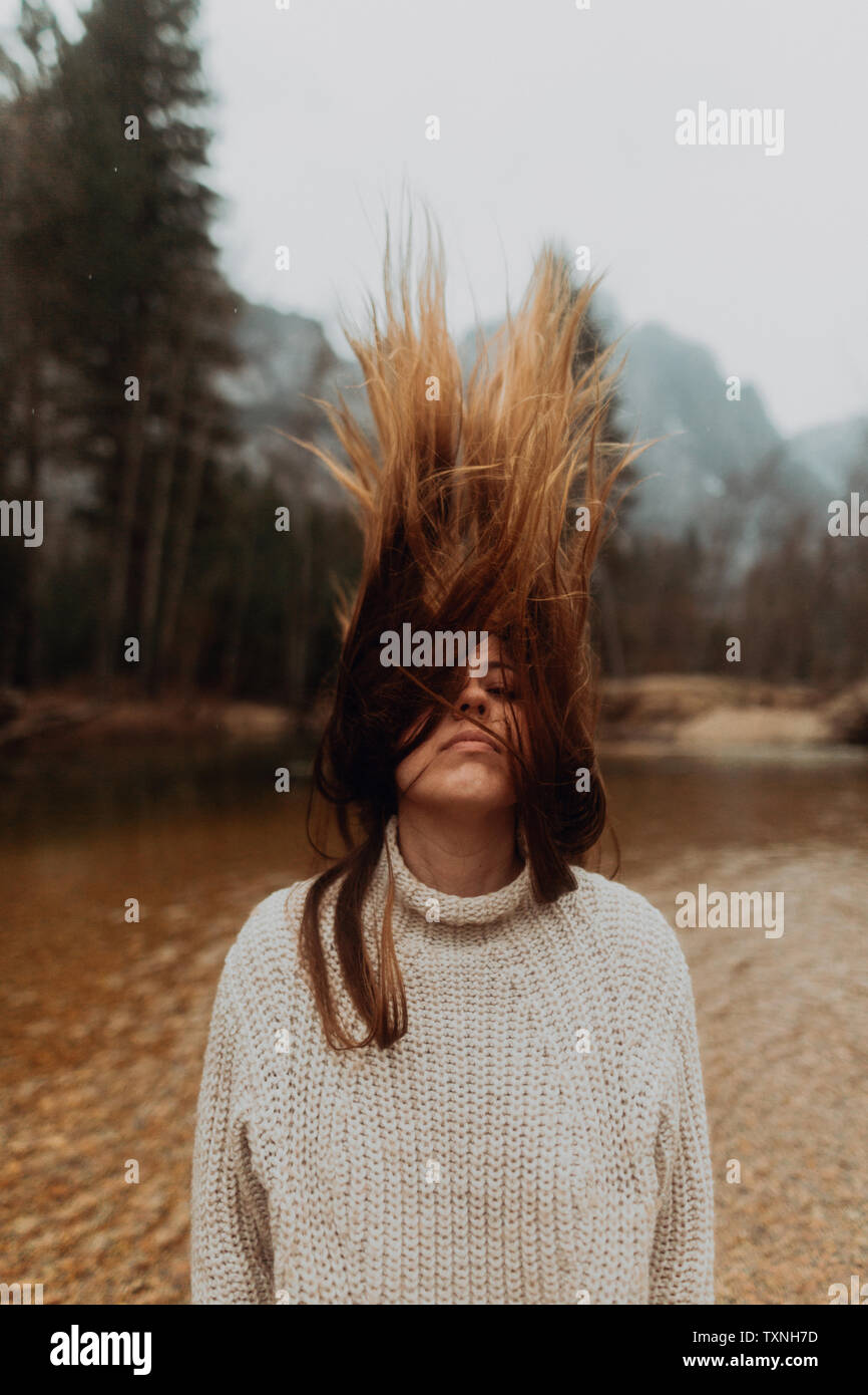 Young woman on riverbank shaking long brown hair, Yosemite Village, California, USA Stock Photo