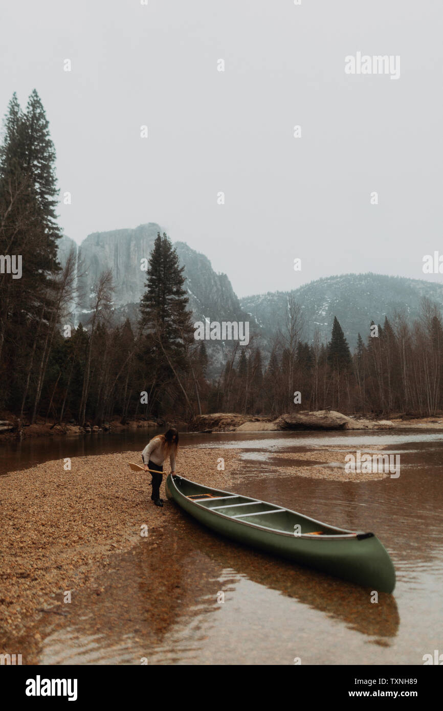 Young female canoeist pulling canoe from river, Yosemite Village