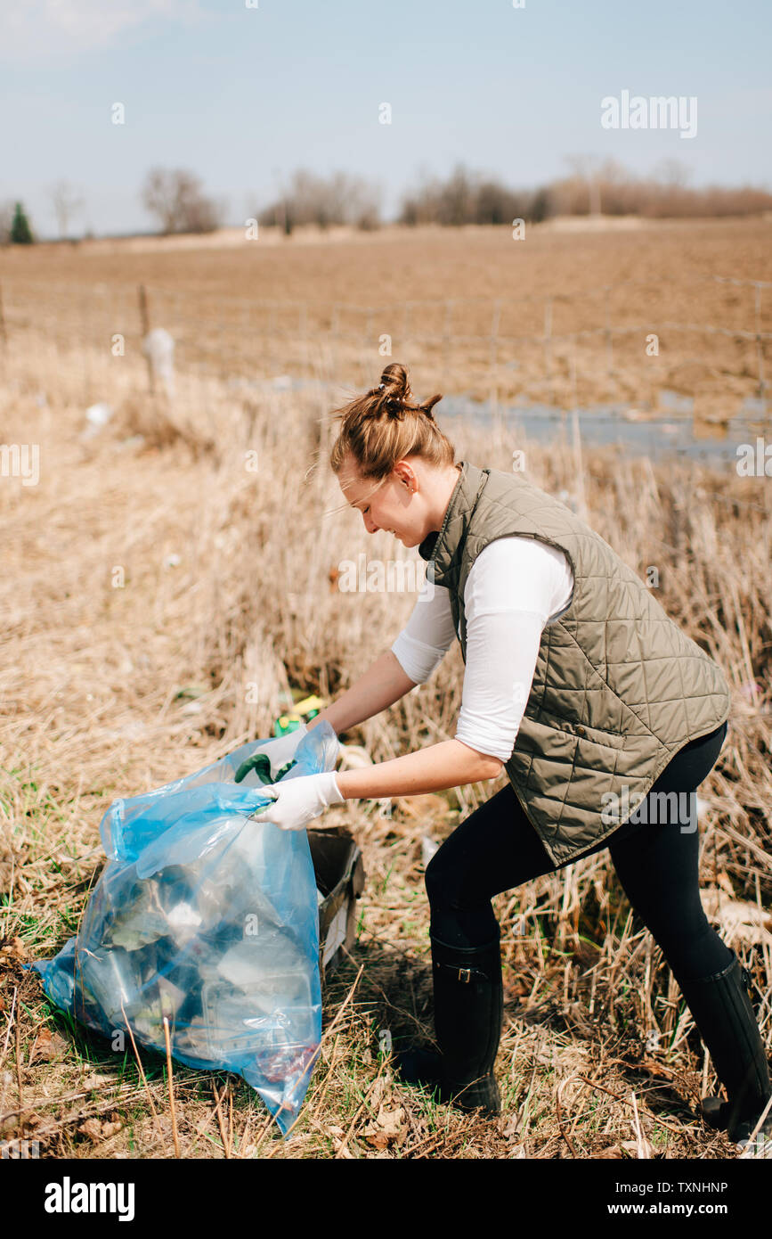 Woman picking up rubbish by field, Georgetown, Canada Stock Photo