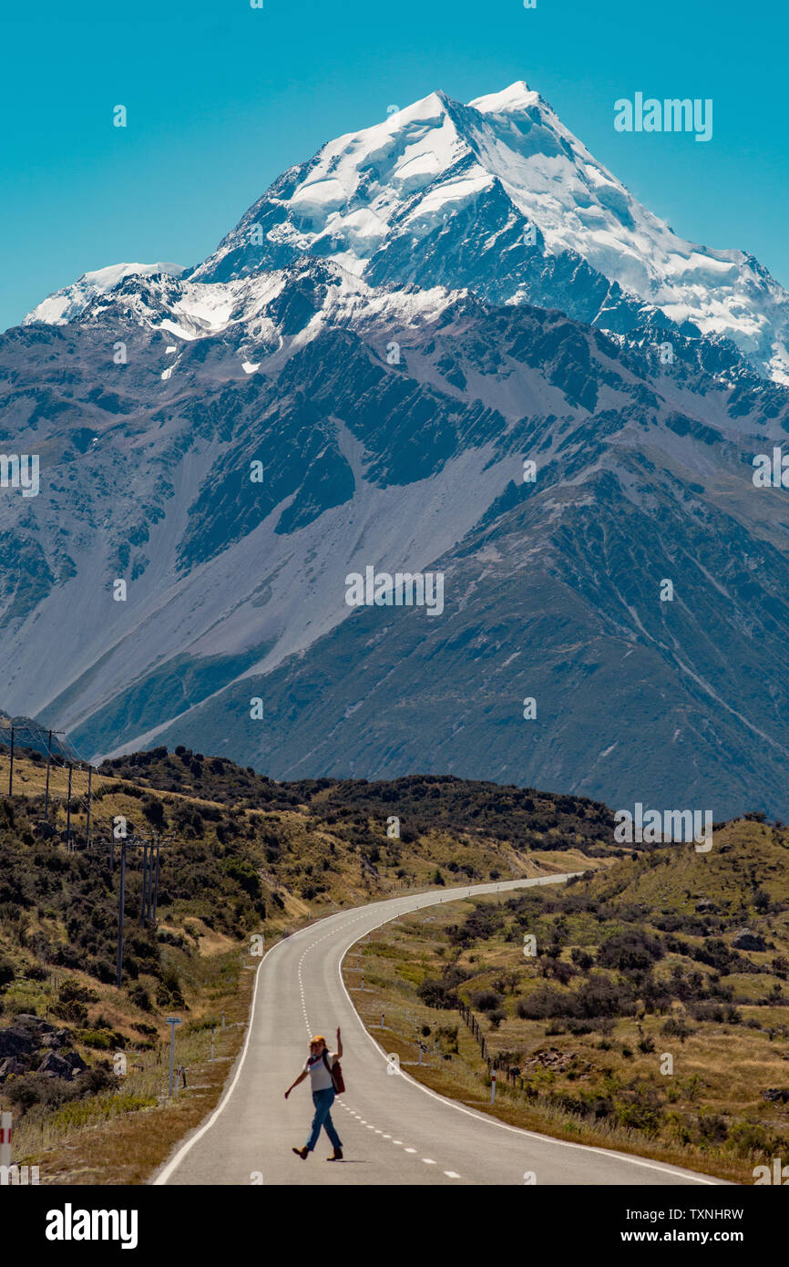 Hiker crossing road leading towards mountains, Wanaka, Taranaki, New Zealand Stock Photo