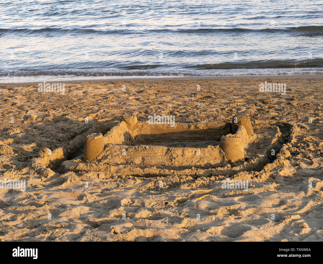 Sandy beach with abandoned sandcastle and waters edge, sea. Warmm sunset. Stock Photo