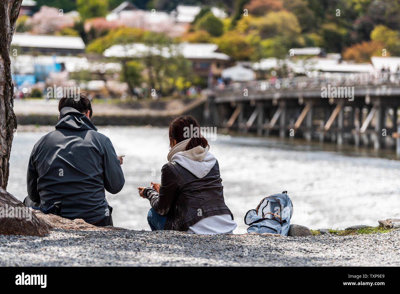 Kyoto, Japan - April 11, 2019: Arashiyama during day with people tourist couple sitting under tree on riverbank in spring and Katsura river Stock Photo