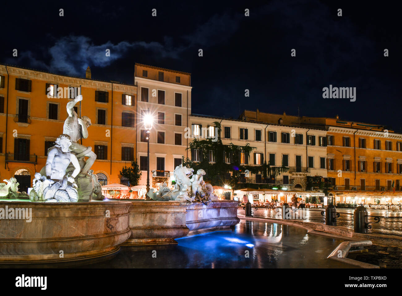The Neptune Fountain is illuminated in the late evening as tourists leave the cafes of the Piazza Navona, in the historic center of Rome, Italy Stock Photo