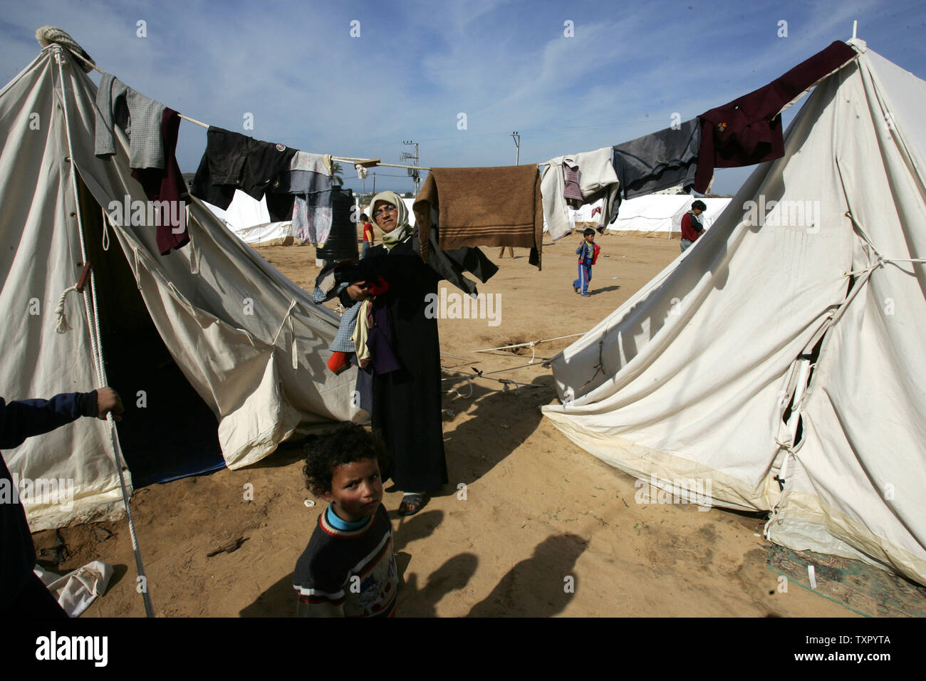 A Palestinian woman hangs laundry on a clothes line between tents ...