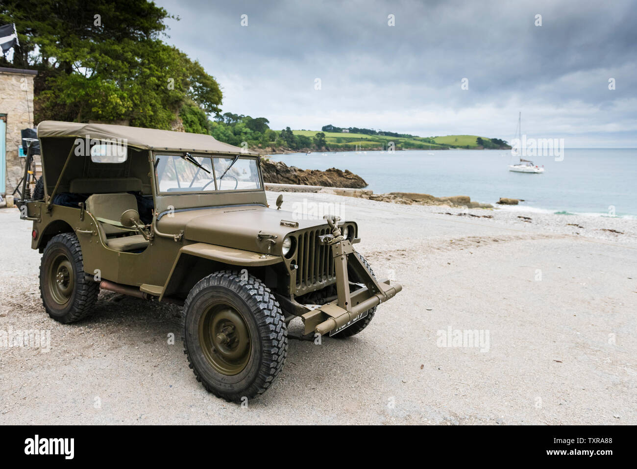 A WWII era Willys Jeep parked on the concrete at Polgwidden Beach in Trebah Garden in Cornwall. Stock Photo