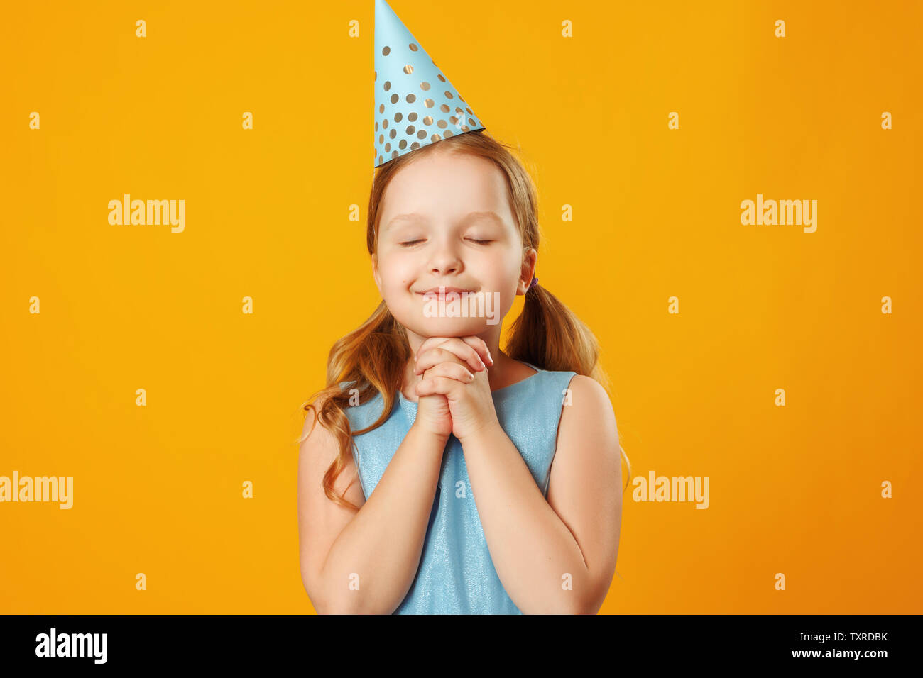 Cute little girl celebrates birthday. The child closed his eyes and made a wish. Closeup portrait on yellow background. Stock Photo